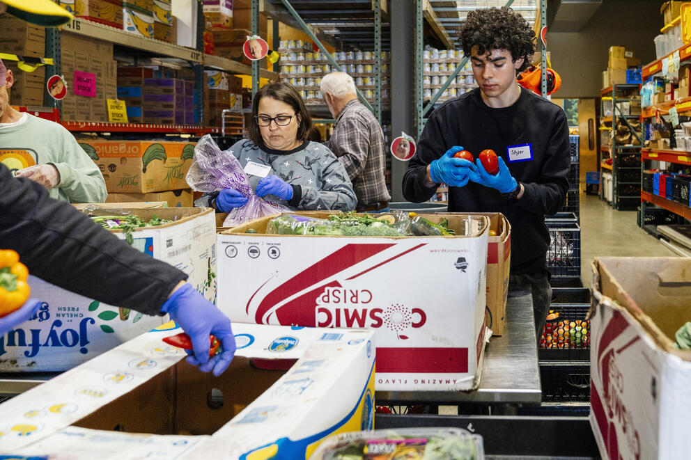 three people sort food in the warehouse of a food bank