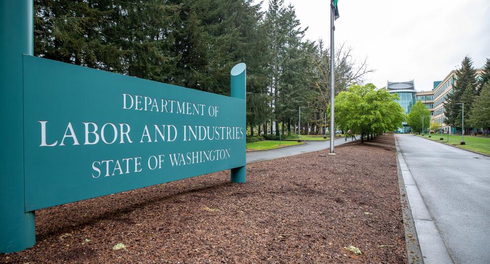 A  large teal sign for the Washington State Department of Labor and Industries marks the entrance to the agency's campus in Tumwater. 