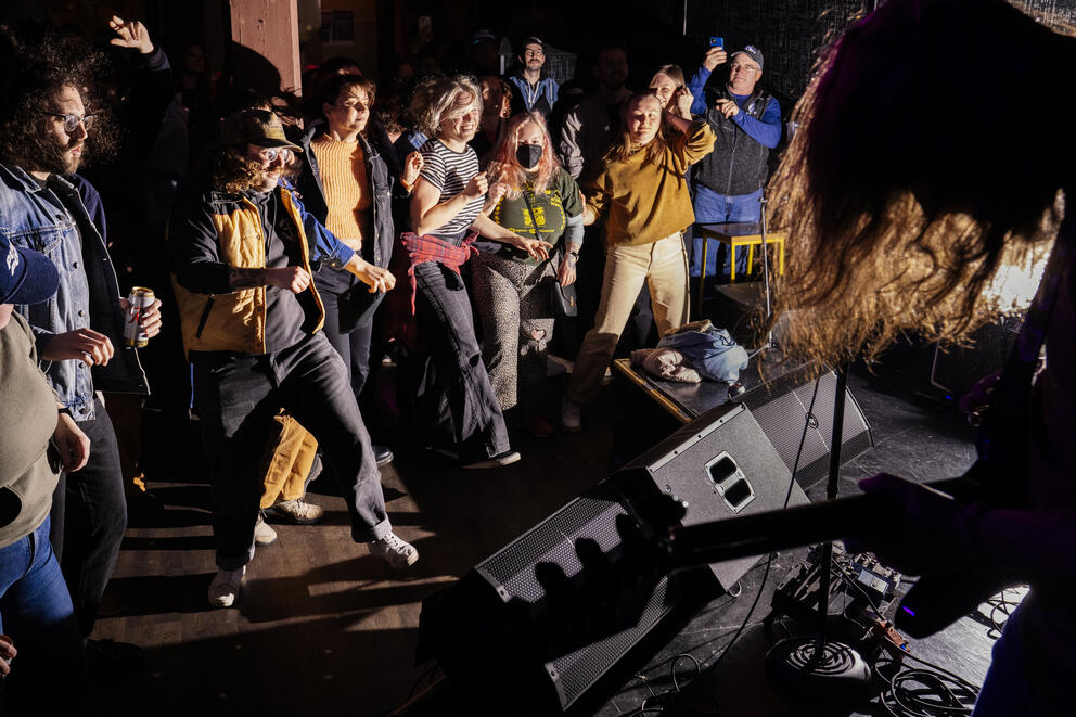 A crowd of people dances on the floor of a music venue. 