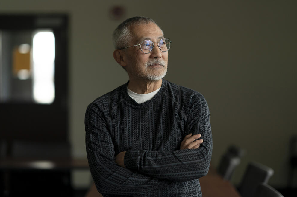 A man looks out to the window inside King County International Airport in Seattle. He's wearing wire glasses, and a gray sweater.