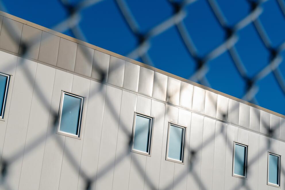 A building with blinds closed is seen through a chain-link fence
