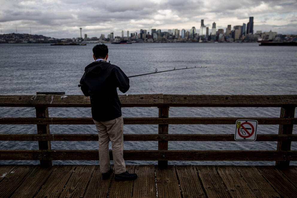 A man stands on a pier while fishing.