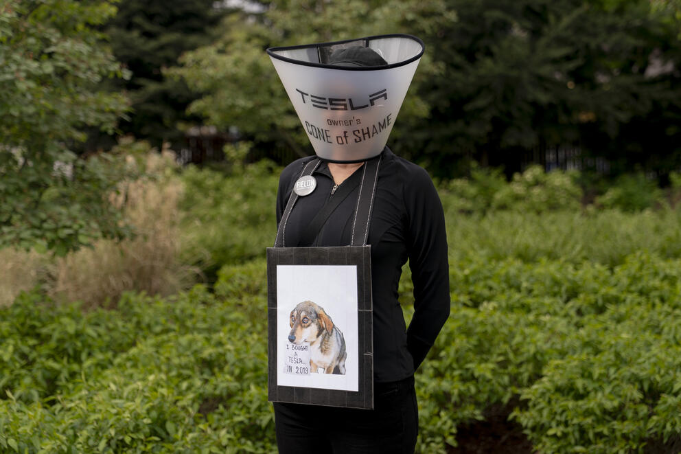 A person wears a pet recovery cone labeled "Cone of Shame"