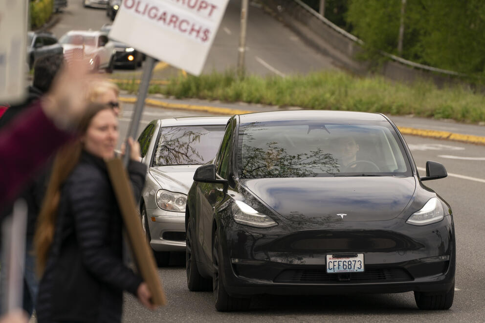 A black car passes several people carrying signs.