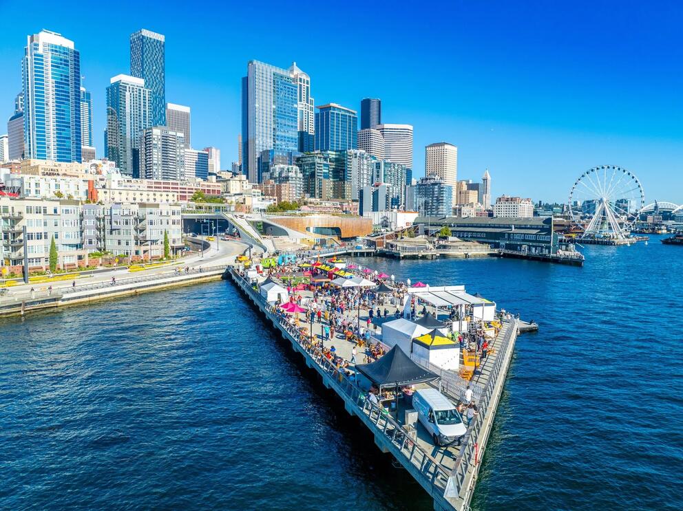 offshore photo of a cityside pier jutting out into the water with tents and people on it