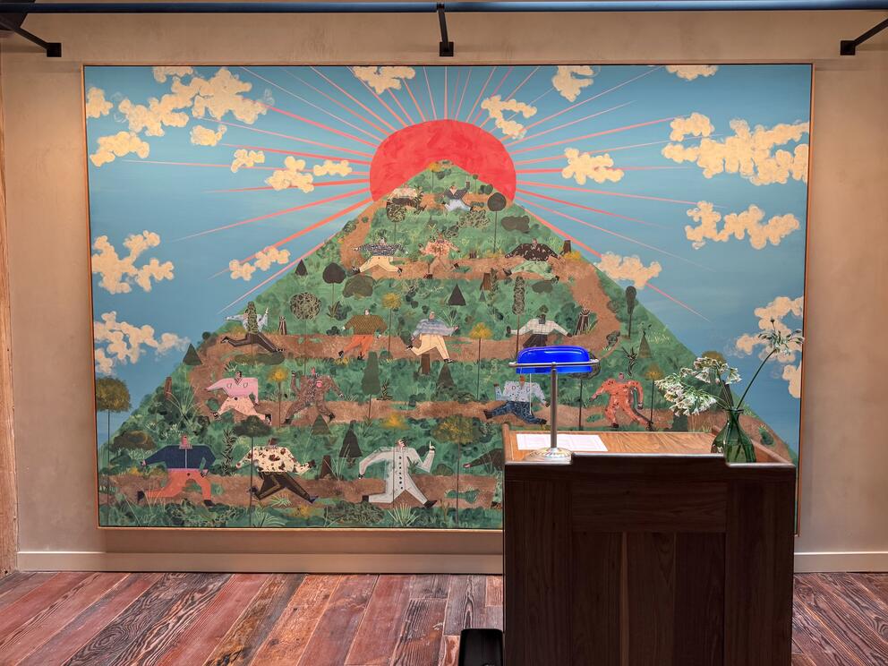 A large painting of a mountain with a cloud-strewn sky in the background hangs on a wall