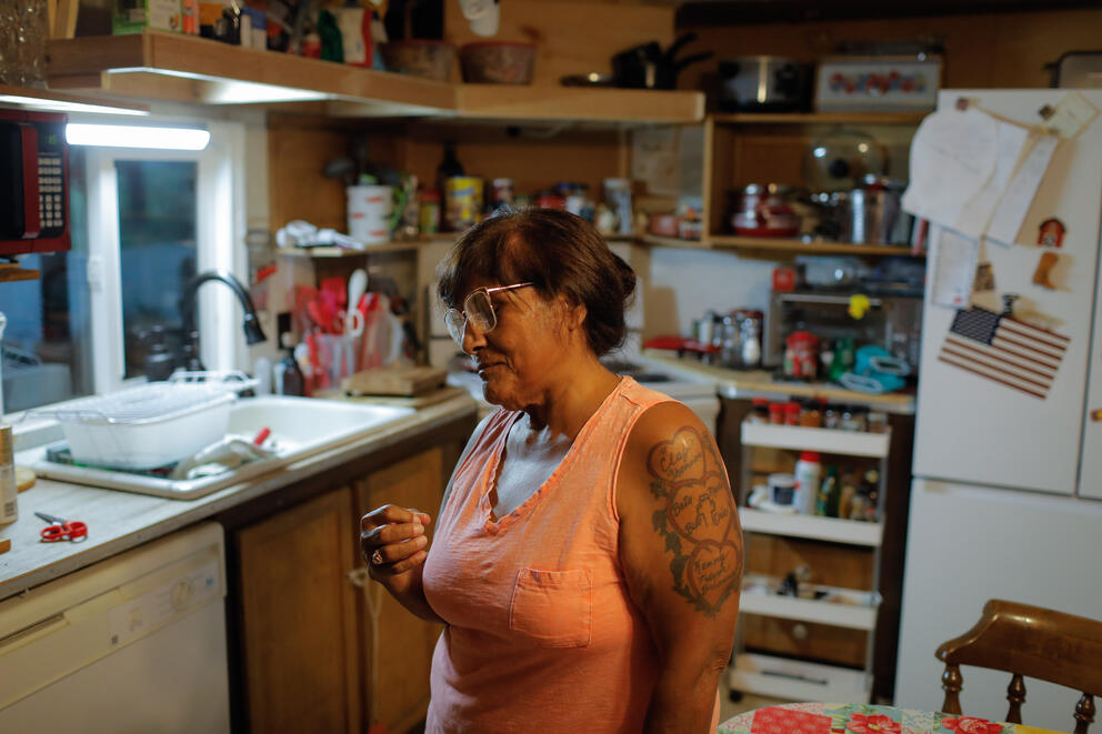 Elva Simmons pictured in her kitchen in Yakima, Washington. She's pictured wearing clear glasses frames and an orange tank top.