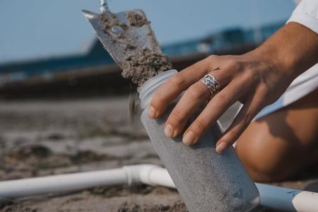 hand with shovel scooping sand into plastic bottle