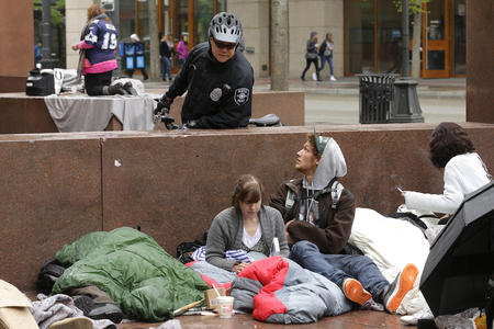 A police officer talking to people sitting on a sidewalk