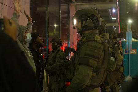 Police in tactical gear talk to demonstrators with their hands up