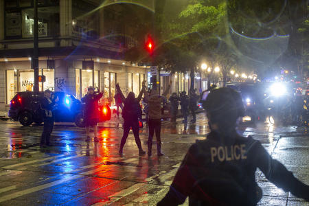 Protesters raise their hands during downtown protest at night, with police nearby