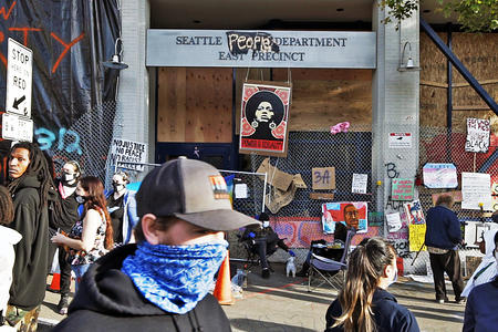 Protesters walk outside an emptied SPD hub. The word "people's" is spray painted over the word "police" on the department's sign