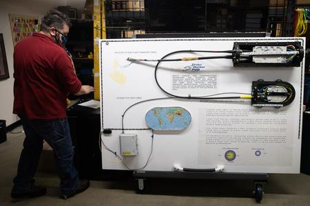 man stands next to board that has explanation of fiberoptic cable and data transmission