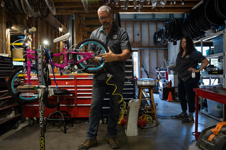 Kelly Campo works on a bike in a shop while Heidi Campo looks on 