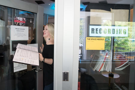 A woman opens a door holding a binder of sheet music