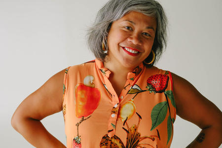 Person with grey short bob wearing a sleeveless orange shirt