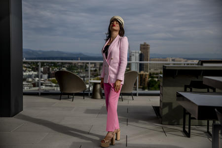 Venus Aoki stands on a rooftop, looking upward, in pink jacket and trousers with cap