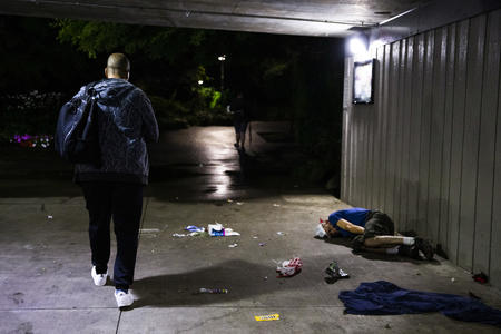 A man walks by a man sleeping on ground
