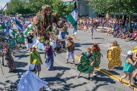 people in a parade wearing turtle costumes with a giant puppet behind them