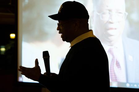 Larry Gossett stands silhouetted in front of a screen that plays one of his campaign videos.