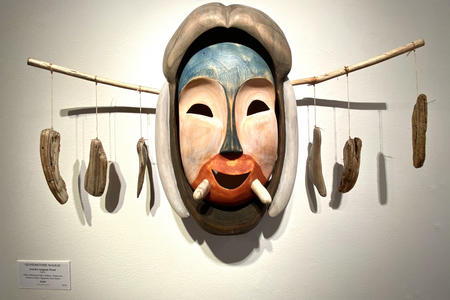 a carved mask with feathers hangin off either side