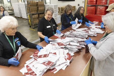A group of women stand around a table sorting through ballots