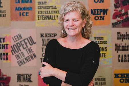 a woman in a black shirt, smiling broadly in front of screen printed posters