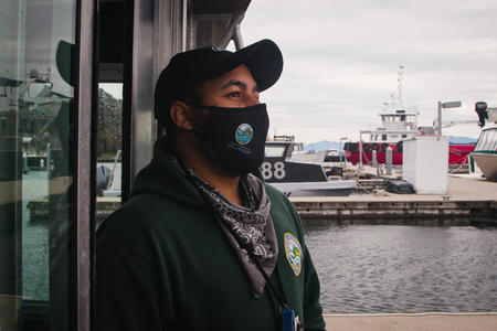man with a face mask standing on boat looking off to the sea