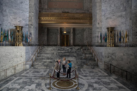 Visitors stand in the rotunda of the state Capitol in Olympia, by a seal of George Washington and surrounded by the Capitol's marble halls.