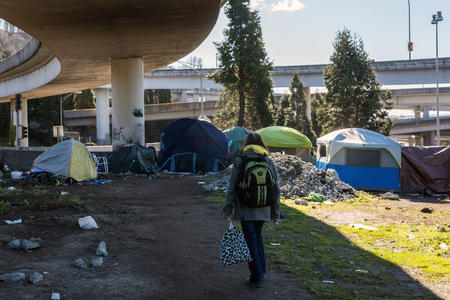a woman walks towards tends under a freeway underpass