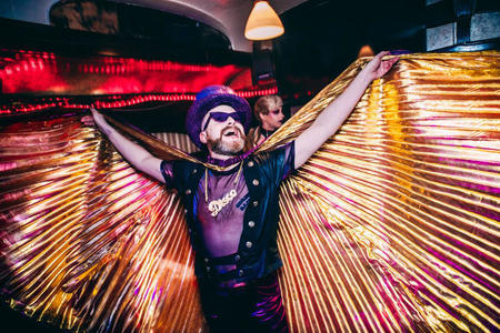 A person with a beard and sunglasses fanning out a long gold cape
