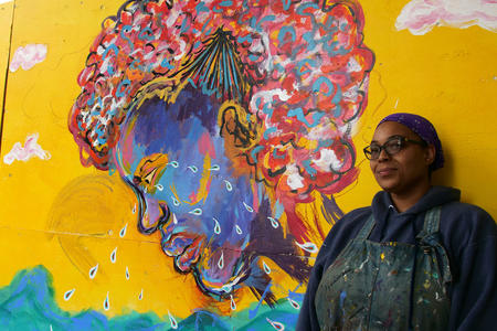 woman stands next to mural