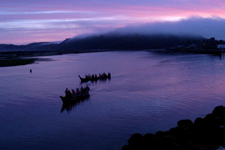 The sunset over the ocean with the silhouettes of paddling canoes