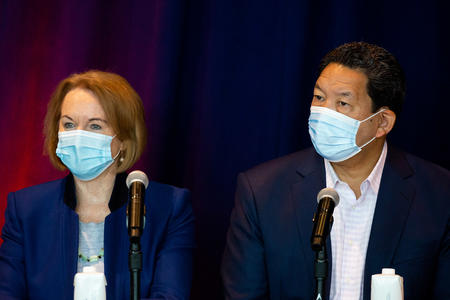former mayor jenny durkan stands next to current mayor bruce harrell both wearing blue surgical masks