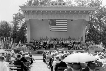 a black and white photo of an old fashioned bandshell with band on stage 
