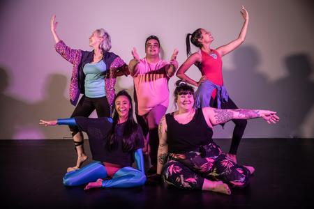 a group of actors in dance outfits strike an exuberant pose