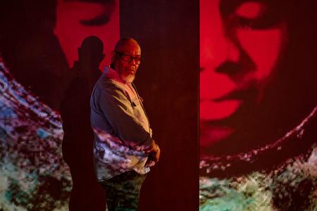 A man stands in front of a projected image of faces