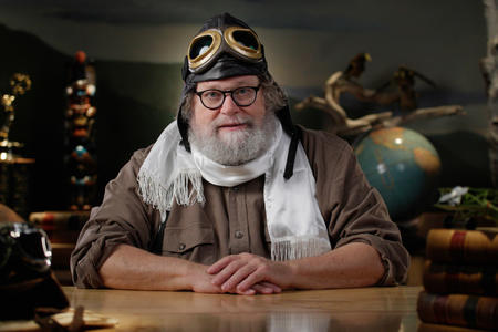 Knute Berger sits at a desk in Mossback's Den wearing World War One pilot gear.