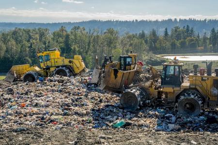 Three bulldozers move trash around a landfill.