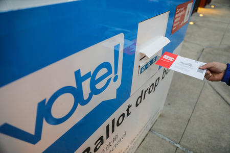 A picture of a voter putting their ballot in a drop box.