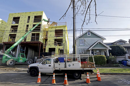 a truck is parked in front of a construction site. an apartment is getting built on the left next to an existing single family home