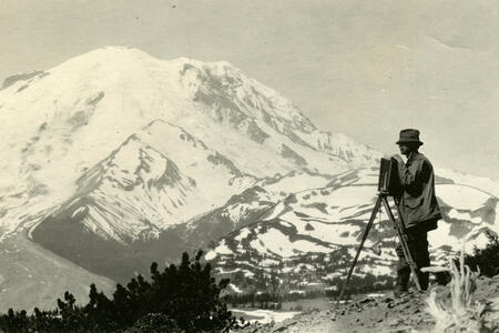 A photographer sets up a vintage camera in the foreground of Mount Rainier