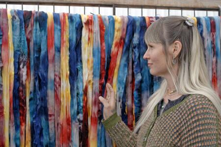 A woman touches a wall of hanging colorful fabrics