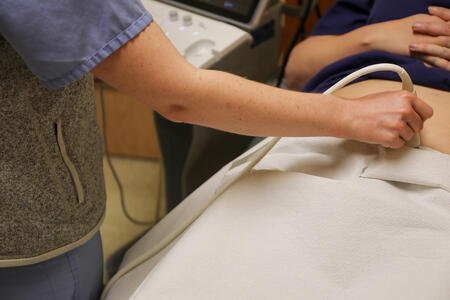 A medical technician holds an instrument to an abdomen.