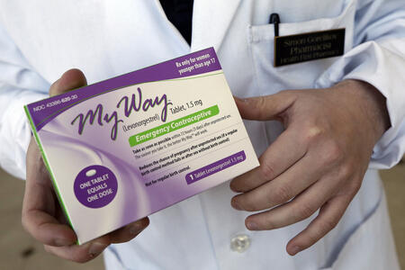 a hand of a pharmacist holding a box of a generic emergency contraceptive