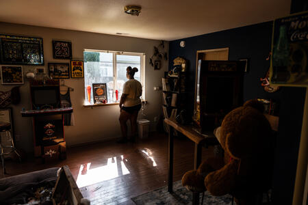 A person looks out of a window of a darkened room.