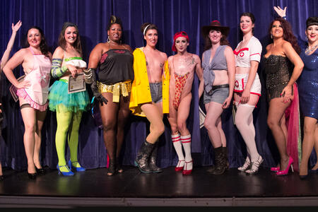 Ten burlesque performers in costume pose on stage.