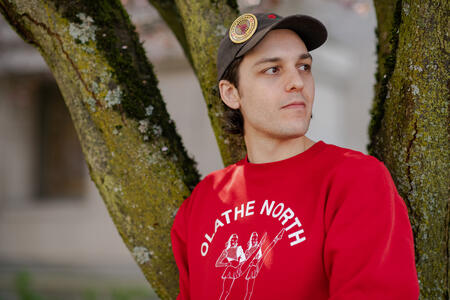 Sean Case stands outside with a red shirt and a pin on his hat that says "Restaurant Workers United" 
