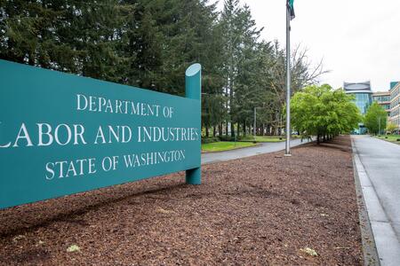 A  large teal sign for the Washington State Department of Labor and Industries marks the entrance to the agency's campus in Tumwater. 