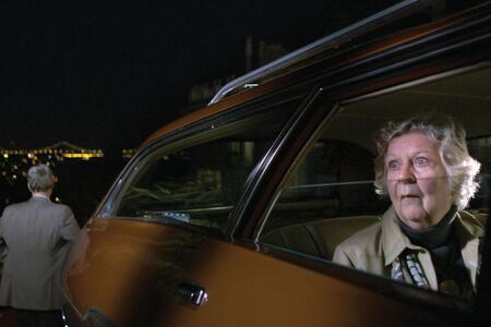 still from a movie in which an elder woman is looking out from a car window in alarm